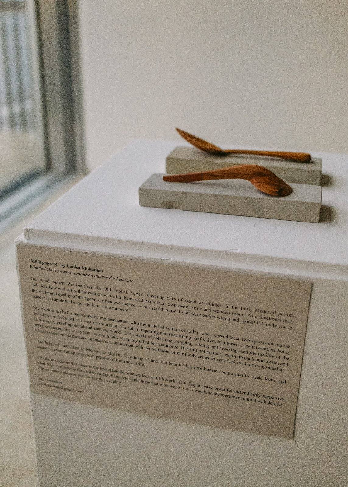Carved wooden spoons displayed on a plinth beside a printed exhibition label.