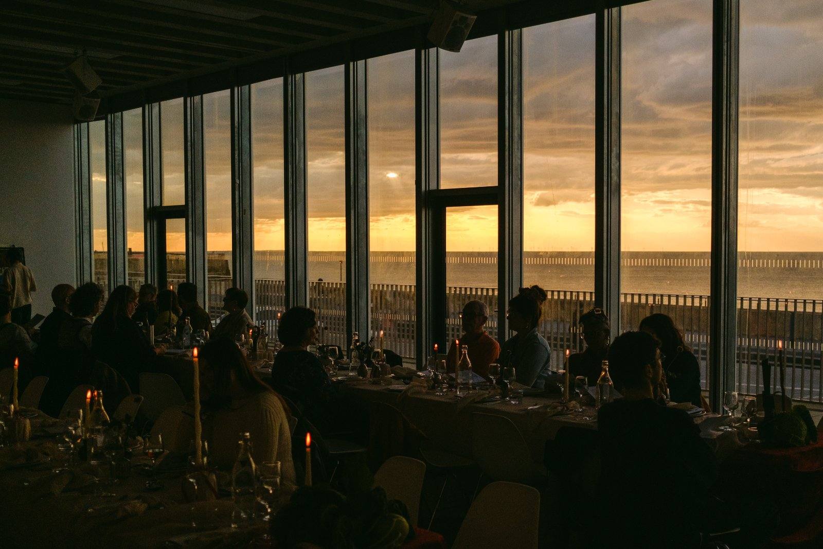 The Foyle Rooms at sunset, long tables of diners silhouetted against floor-to-ceiling windows over the sea.