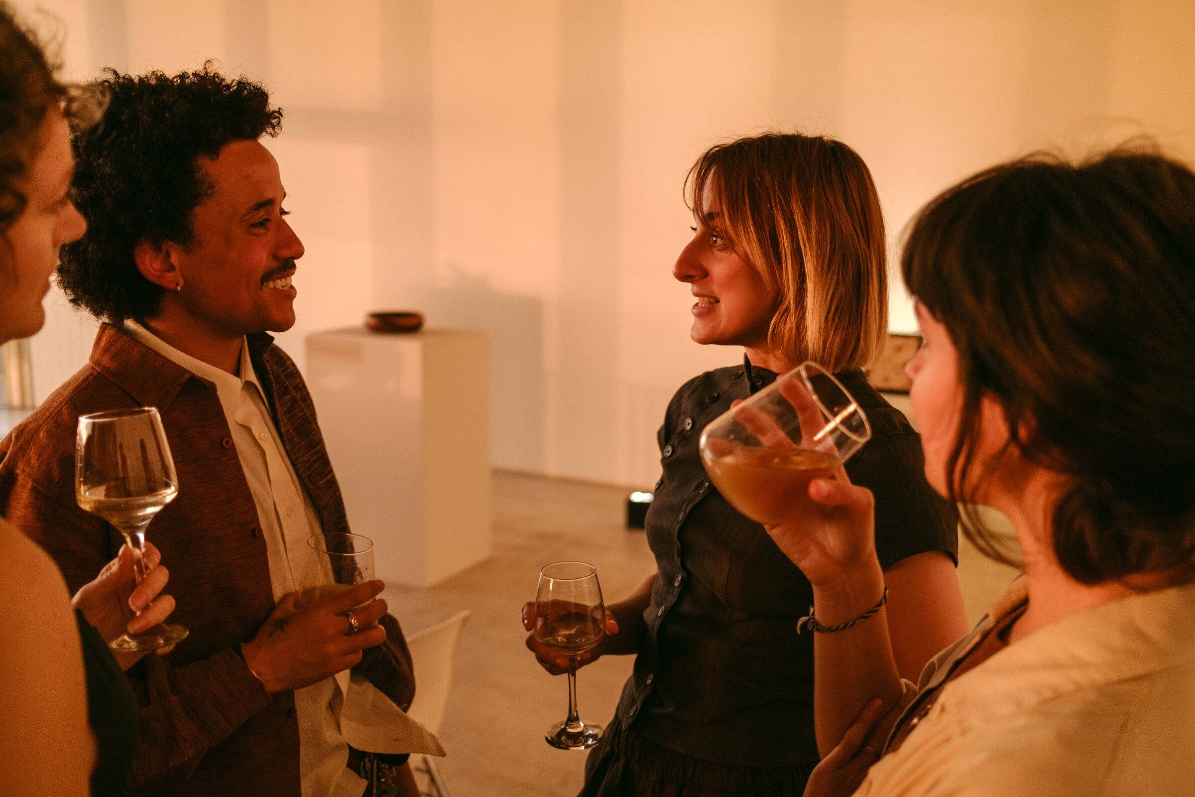 Guests talking and holding glasses of wine in warm evening light.