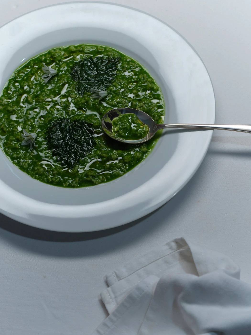 A bowl of vivid green soup with a spoon resting in it.