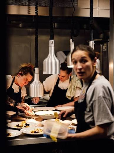 Louisa and other chefs plating dishes at the pass of a busy restaurant kitchen.