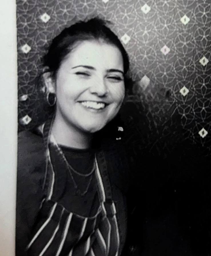 Black and white portrait of Louisa Mokadem smiling, wearing a striped apron.